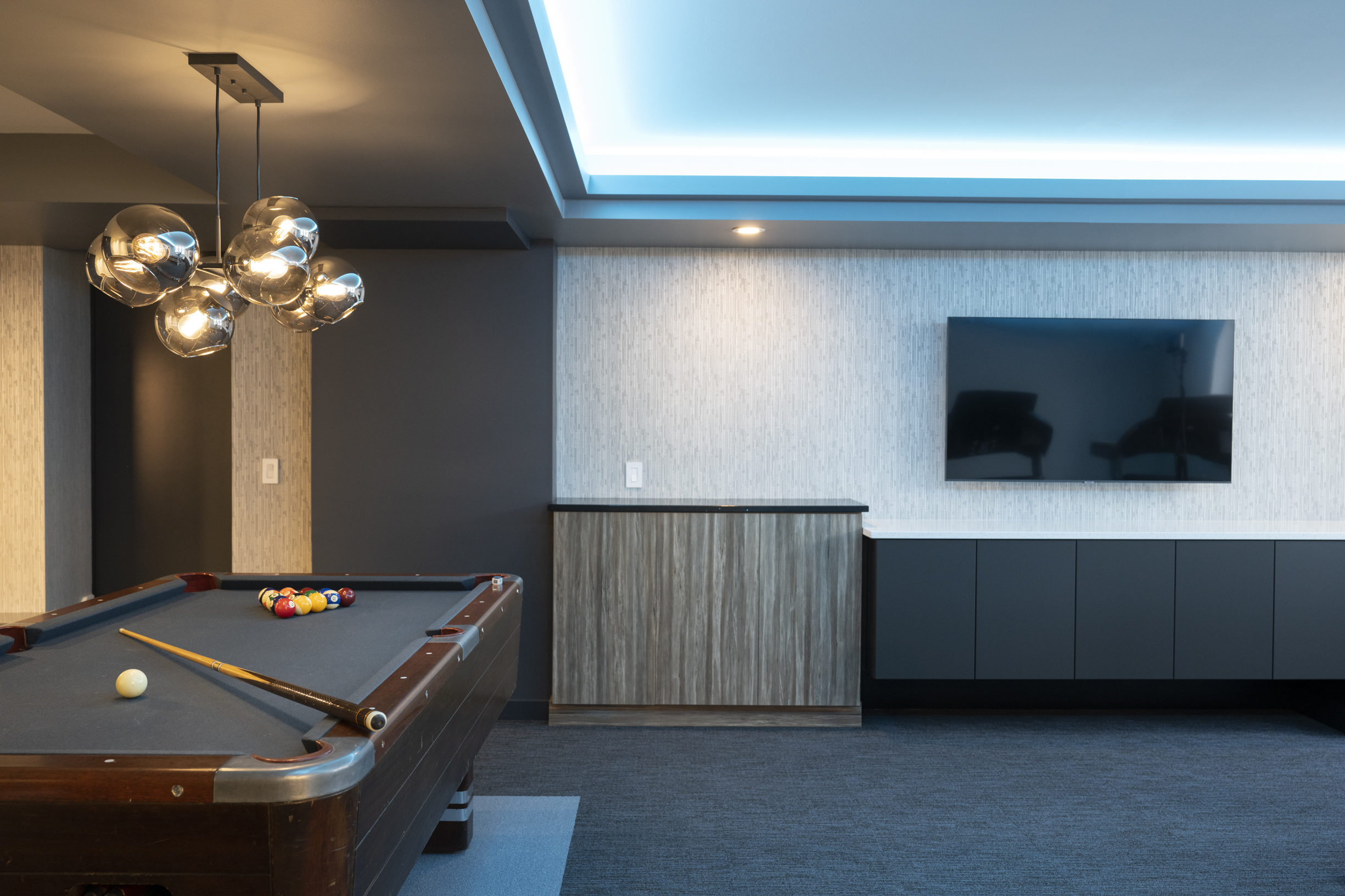 basement remodel with pool table, lights that change color along the ceiling, and unique, modern light fixture